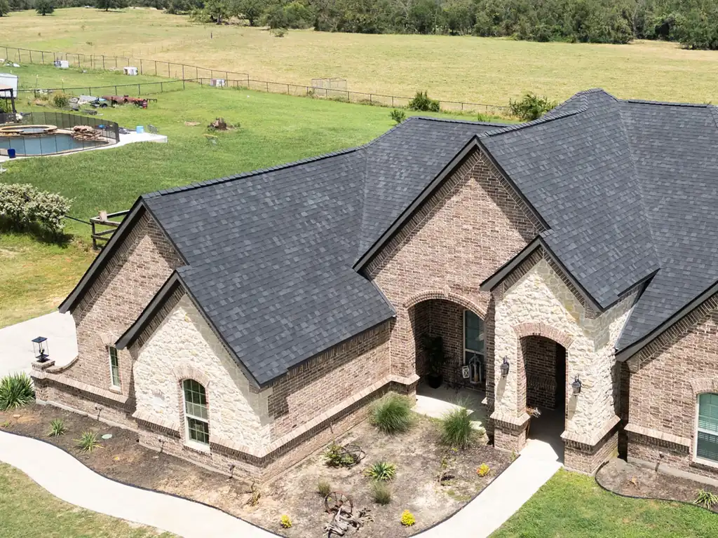 A Parker County brick and stone home seen from above, its new charcoal architectural shingle roof taking up most of the picture and the yard left clean